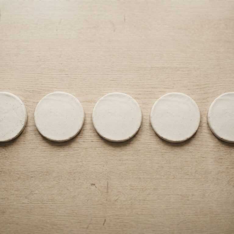 Five finished pale clay discs resting on a wooden table in daylight