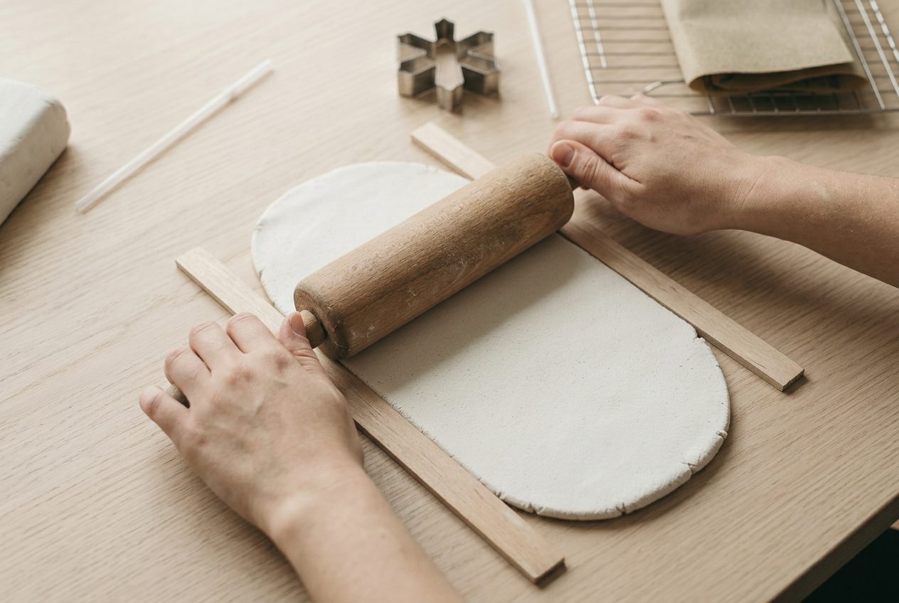 A rolling pin flattening white clay between two wooden strips