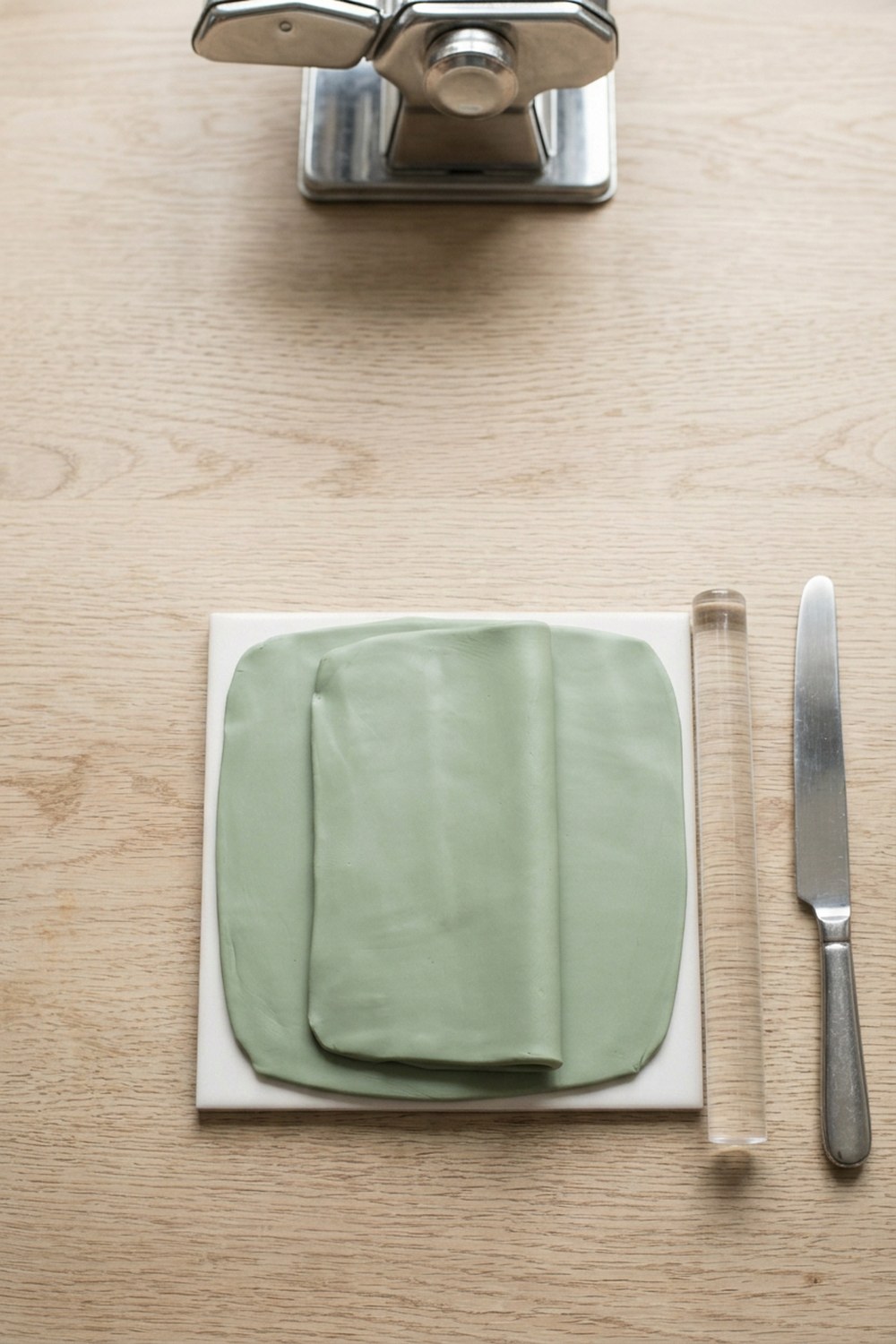Polymer clay being rolled and folded on a white ceramic tile