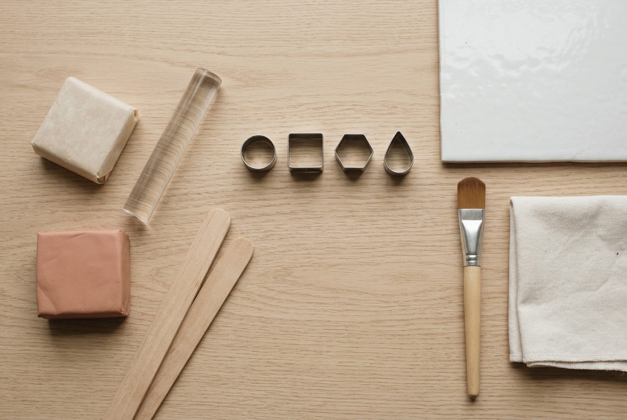 A row of small metal cutters, a roller and a soft brush on a white tile