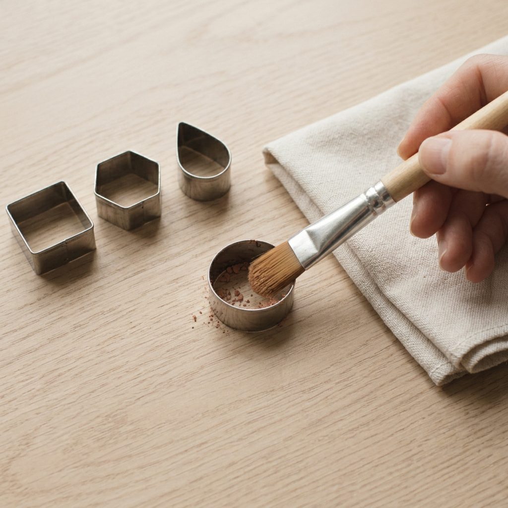 A soft brush clearing clay crumbs from inside a small metal cutter