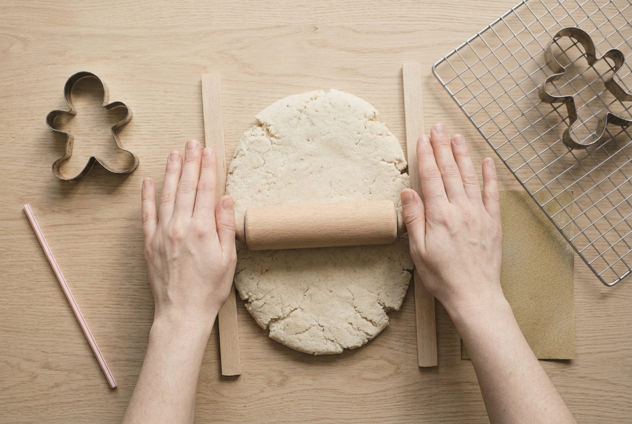 A rolling pin flattening the dough between two wooden guide strips