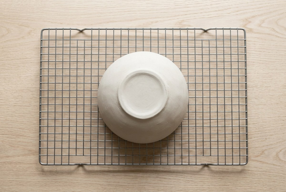 A pale clay bowl drying on a wire rack in soft daylight
